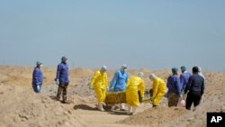 FILE - Iraqi health ministry workers carry a coffin of a person who died from coronavirus infection at a new cemetery for people who died from COVID-19, outside the town of Najaf, Iraq, March 30, 2020.