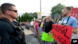 Watched by police, demonstrators against the Senate Republican health care bill await the arrival of Pennsylvania's U.S. Sen. Pat Toomey outside the studios of WHTM-TV, July 5, 2017 in Harrisburg, Pa.