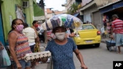 A woman wearing a protective face mask carries food donated by “Eu sou Eu” or “I am me,” a non-profit run by former inmates, during the coronavirus pandemic, at the Para-Pedro favela in Rio de Janeiro, Brazil, May 8, 2020.