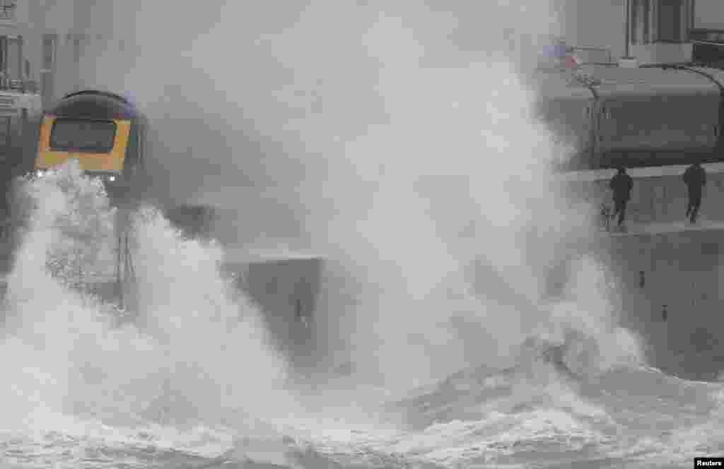 Large waves hit the sea wall as Storm Brendan bringing high winds and heavy rain, while a train passes through Dawlish, southwest Britain.