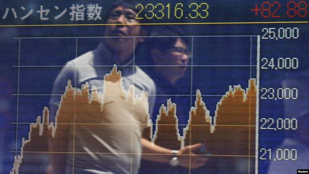 FILE - Passersby are reflected on in electronic graph showing recent movements of the Hang Seng Index outside a brokerage in Tokyo.