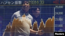 FILE - Passersby are reflected on in electronic graph showing recent movements of the Hang Seng Index outside a brokerage in Tokyo.