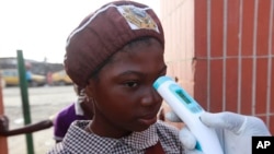 FILE - A teacher uses a thermometer to test students' temperature checking for signs of Ebola virus at Aiyetoro African Church Nursery and Primary school in Lagos, Nigeria.