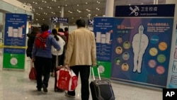 In this Jan. 13, 2020, photo, travelers pass by a health checkpoint before entering immigration at the international airport in Beijing. The possibility that a new virus in central China could spread between humans cannot be ruled out, though the…