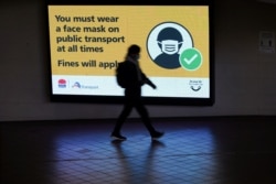 FILE - A person walks past a public health warning for passengers to wear face masks at a city center transit station during a lockdown to curb the spread of COVID-19 in Sydney, Australia, August 17, 2021.