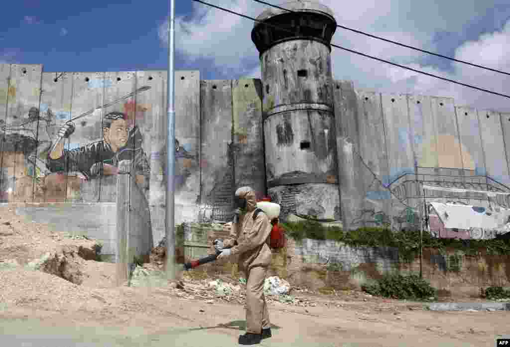 A Palestinian sanitary department worker sprays disinfectant around the refugee camp of Aida, in Bethlehem which has been under lockdown for more than a week due to the novel coronavirus epidemic.