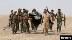 Iraq's Shi'ite paramilitaries and members of Iraqi security forces hold an Islamist State flag which they pulled down in Nibai, in Anbar province, May 26, 2015.