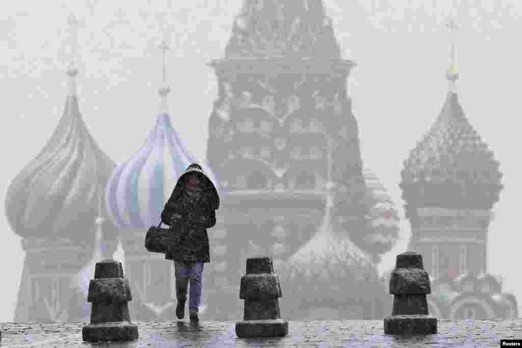 A woman walks along Red Square under snowfall, with St. Basil&#39;s Cathedral seen in the background, in central Moscow, Russia.