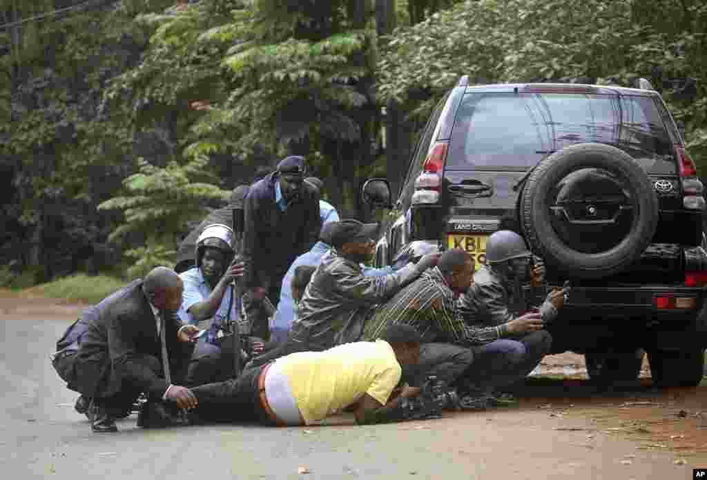 Kenyan security personnel and journalists duck behind a vehicle as heavy gunfire erupts from the Westgate Mall in Nairobi Kenya, Sept. 23 2013.