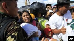 Una mujer con su hijo en brazos suplica ser evacuada en medio de una multitud de damnificados en Tacloban.