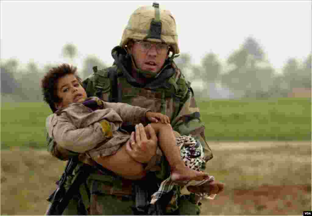 Gizir Joseph Patrick Dwyer-in bu fotosu 2003-cü il, martın 25-i çəkilib. Bağdaddan cənubda yerləşən Mişkab şəhərində həbrbçi oğlan uşağını təhlükəsiz yerə qaçırır.&nbsp; Dwyer 2008-ci ilin iyulunda dərman dozasının çoxluğundan dünyasını dəyişib.&nbsp; Foto: ARMY TIMES/ WARREN ZINN via CBS News.