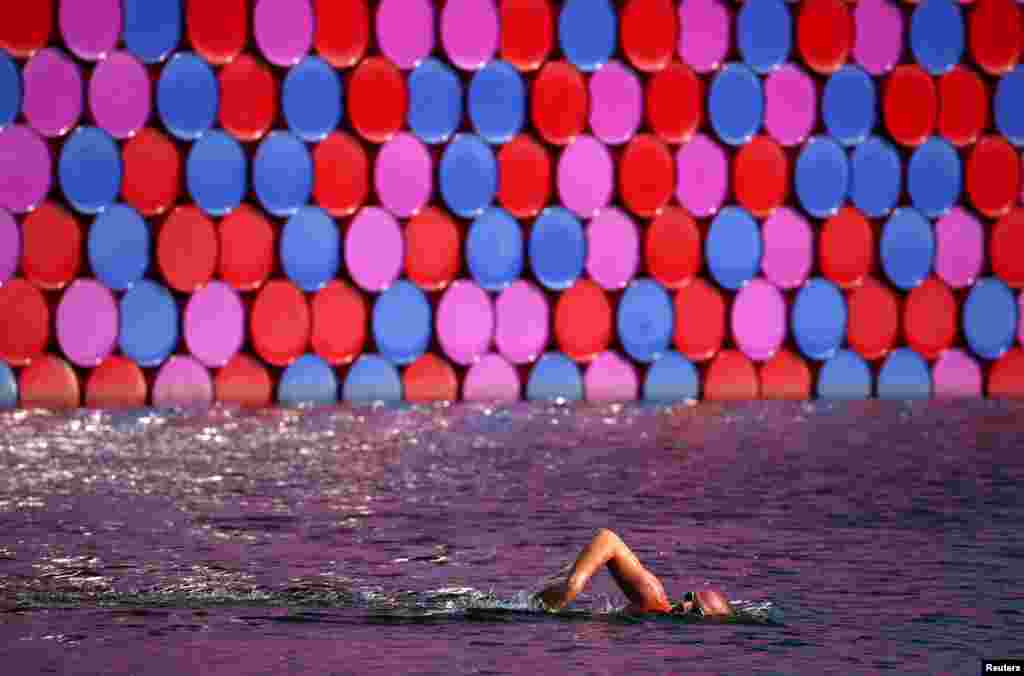 Seorang pria berenang melewati patung mengambang &quot;The London Mastaba&quot; di Serpentine, London, Inggris.