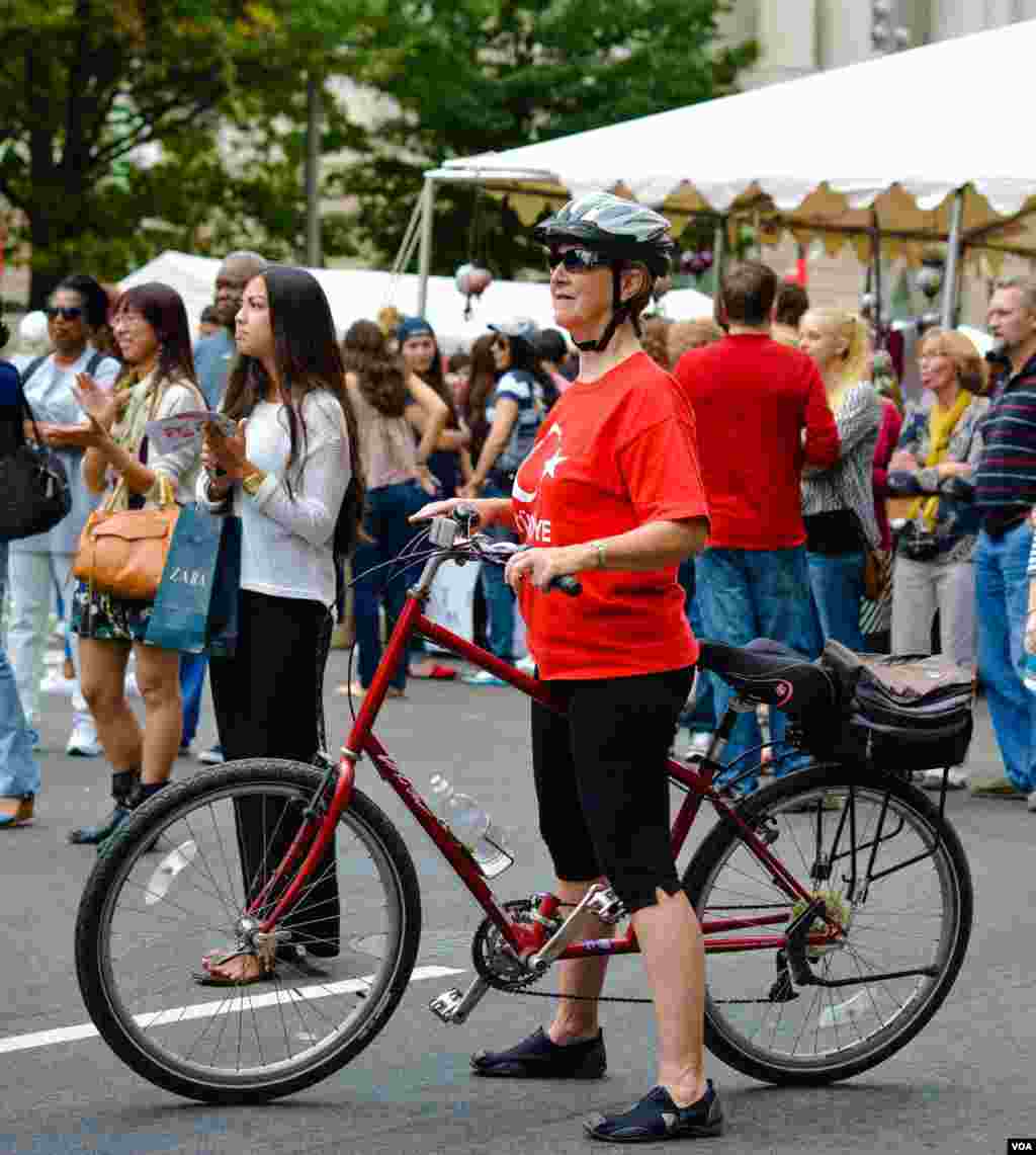 Turkcha futbolka kiygan velosipedchi ayol raqs dasturini tomosha qilmoqda, Vashingtondagi turk festivalidan, 29-sentabr, 2013-yil