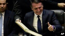 Brazil's President Jair Bolsonaro, right, smiles after signing the official record to become President, as his Vice President Hamilton Mourao, left, looks on during their inauguration, in the plenary of the Brazilian National Congress, in Brasilia, Jan. 1