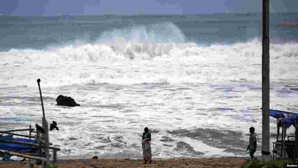 People stand as waves from the Bay of Bengal approach the shore in Visakhapatnam district in the southern Indian state of Andhra Pradesh on October 12, 2013.