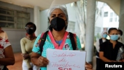 Trabajadora de la salud sostiene un cartel que dice "Salarios de hambre, SOS Salud" durante una protesta por la falta de vacunas contra COVID-19 y por mejores salarios en el Hospital Universitario de Caracas, el 7 de abril de 2021.