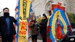 Maro Park, left, of Fairfax, Virginia, holds a sign saying "Congress Must Act Now," next to Paola Marquez and LaRia Land, both of Silver Spring, Maryland, as they stand by a banner of the Lady of Guadalupe, during a march with others in support of the Deferred Action for Childhood Arrivals (DACA) program, on Capitol Hill, Dec. 12, 2017, in Washington. 