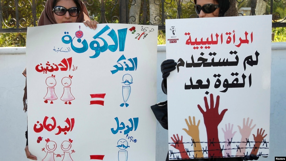 Dua perempuan memegang poster dalam sebuah unjuk rasa di Tripoli. Poster di kiri berbunyi: Karena dua perempuan sama dengan satu lelaki (dalam hukum Shariah), maka harus ada dua perempuan dalam setiap satu lelaki di parlemen, untuk membuat formula ini tepat (7/2/2012).