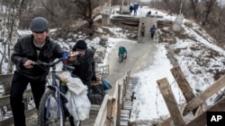 Local residents walk across a bridge damaged during fighting between Ukrainian government forces and Russia-backed rebels in Stanytsia Luhanska, Luhansk region, eastern Ukraine, Jan. 16, 2016.