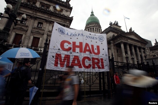 FILE - Argentine unions, small firms and activists gather outside Argentina's Congress to demand changes in President Mauricio Macri's economic policies, in Buenos Aires, Argentina, April 4, 2019. The banner reads "Bye Macri."