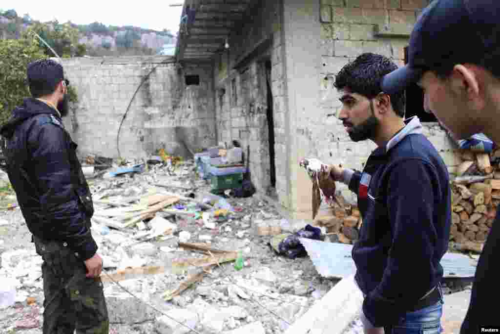 A Free Syrian Army fighter holds a dead bird as his comrades inspect the damage caused by what activists said were barrel bombs dropped by government forces in Jabal al-Akrad, Latakia, Jan. 23, 2014.