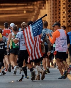 Seorang pelari membawa bendera Amerika Serikat saat dia melintasi Jembatan Queensboro selama Maraton Kota New York di New York, Minggu, 4 November 2018. (Foto: AP/Andres Kudacki)
