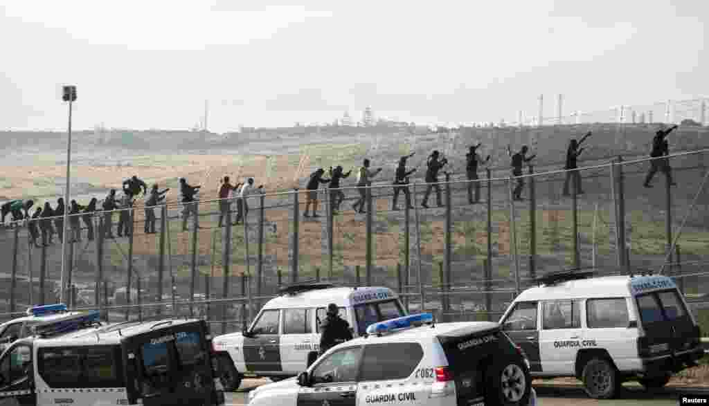 African migrants walk along a border fence covered in razor wire as Spanish Civil Guard vehicles are positioned in front of them, during their latest attempt to cross into Spanish territory between Morocco and Spain&#39;s north African enclave of Melilla.