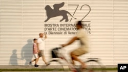 People pass by the logo of the 72nd edition of the Venice Film Festival, at the Venice Lido, Aug. 31, 2015. 