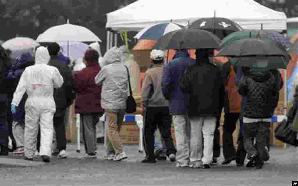 Officials wearing clothing to protect against radiation directs people to a center to scan residents who have been within 20 kilometers of the Fukushima Dai-ichi nuclear plant damaged by Friday's earthquake Tuesday, in Koriyama, Fukushima Prefecture, Jap