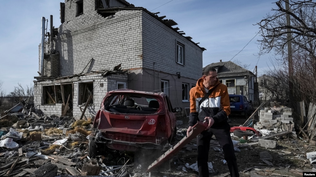 Bir bölge sakini, Rusya'nın Ukrayna'ya saldırısı sırasında, Dnipro, Ukrayna'da, 26 Şubat 2024'te, Rus insansız hava aracı saldırısı sırasında hasar gören bir konut binasının yakınında, hasarlı bir arabayı çekilmek üzere hazırlıyor.