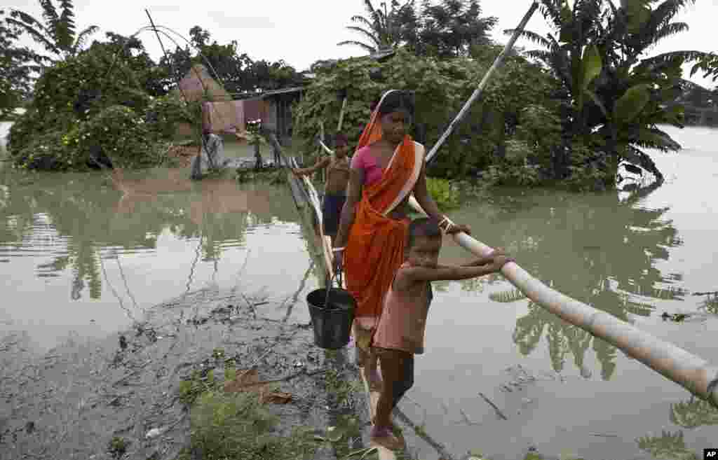 Warga lokal yang terkena dampak hujan berjalan di jembatan darurat di desa Mayong, sekitar 55 kilometer Gauhati timur, India.