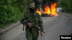 Un separatista prorruso vigilan en un retén en las afueras de Slaviansk, en Ucrania oriental. En el fondo arden unas llantas de automóvil.