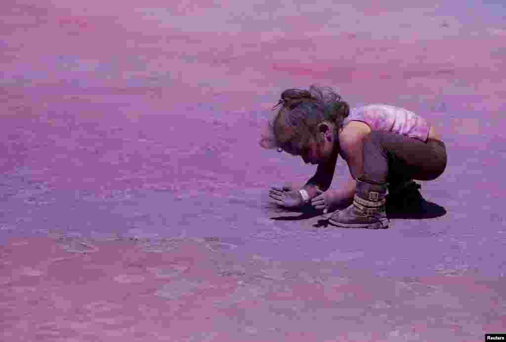 یک کودک هندی در حال جمع کردن رنگ از زمین که در آن لحظات پیش جشن هولی برگزار گردیده بود.