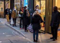 People with a protective masks line up using social distancing to queue at a supermarket in Paris, March 16, 2020.