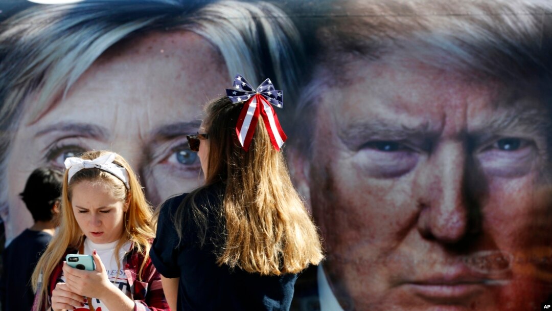 Dua anak perempuan berdiri dekat bus yang menampilkan dua foto raksasa para capres AS, Hillary Clinton dan Donald Trump, di Hempstead, New York (26/9). (AP/Mary Altaffer)