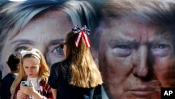 Dua anak perempuan berdiri dekat bus yang menampilkan dua foto raksasa para capres AS, Hillary Clinton dan Donald Trump, di Hempstead, New York (26/9). (AP/Mary Altaffer)