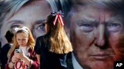 FILE - Girls pause near a bus displaying large photos of candidates Hillary Clinton and Donald Trump before the presidential debate at Hofstra University in Hempstead, New York, Sept. 26, 2016.
