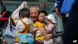 An elderly man plays with children near a commercial office building in Beijing on May 10, 2021. 