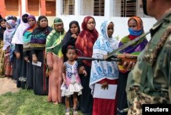 A girl looks at an armed security person standing guard as her mother waits in a queue to cast her vote outside a polling station during the sixth phase of general election in Sepahijala district in the northeastern state of Tripura, India, May 12, 2019.