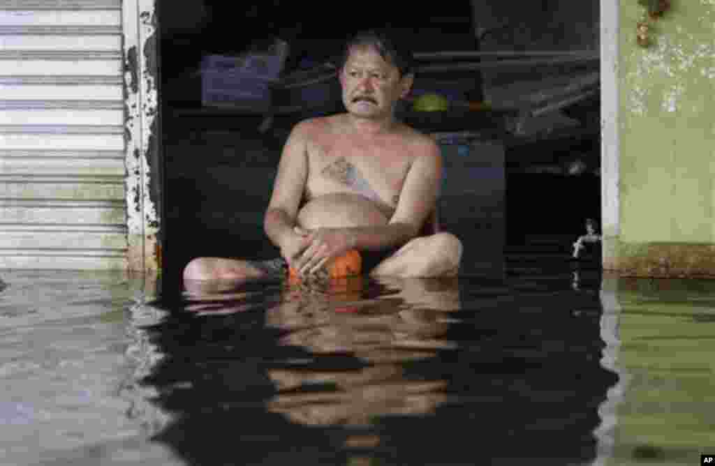 A Thai man sits outside his flooded house in Bangkok, Thailand on Wednesday Nov. 9, 2011. The flooding began in late July and the water has reached parts of Bangkok, where residents are frustrated by government confusion over how much worse the flooding w
