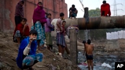 FILE - Indian men attend to their morning chores next to a sewage canal before they leave for work early morning in New Delhi, India, Dec. 12, 2014.