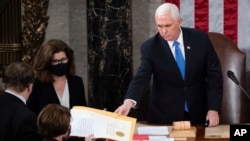 FILE - Then-U.S. Vice President Mike Pence hands an electoral certificate to Senator Amy Klobuchar as he presides over a joint session of Congress as it convenes to count the Electoral College votes cast in the 2020 presidential election, in Washington on Jan. 6, 2021.