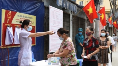 Người dân được kiểm tra thân nhiệt khi xếp hàng chờ bỏ phiếu tại một điểm bầu cử hôm 23/5 dù Việt Nam đang trải qua cao điểm của đợt bùng phát mới trong cộng đồng. Con số ca lây nhiễm mới trong ngày đạt kỷ lục hôm 16/6 với 423 người dương tính với COVID-19.