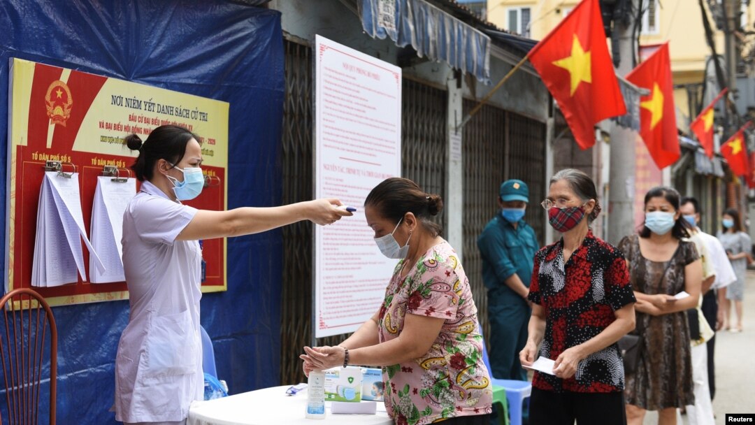 Người dân được kiểm tra thân nhiệt khi xếp hàng chờ bỏ phiếu tại một điểm bầu cử hôm 23/5 dù Việt Nam đang trải qua cao điểm của đợt bùng phát mới trong cộng đồng. Con số ca lây nhiễm mới trong ngày đạt kỷ lục hôm 16/6 với 423 người dương tính với COVID-19.