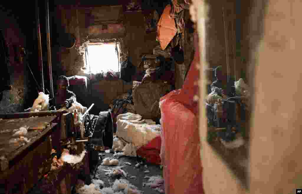 An Afghan laborer uses machinery to fluff raw cotton of a bale to make pillows and mattresses, at his traditional shop in Kabul.