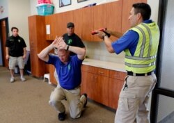 Police officers David Riggall, kneeling, and Nick Guadarrama, right, instruct students Bryan Hetherington, left rear, and Chris Scott, center rear, during a security training session at Fellowship of the Parks campus in Haslet, Texas, July 21, 2019.