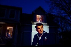 An image of veteran Stephen Kulig is projected onto the home of his daughter, Elizabeth DeForest, as she looks out the window of a spare bedroom as her husband, Kevin, sits downstairs in Chicopee, Mass., May 3, 2020.