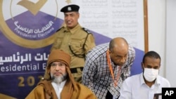 Саїф аль-Іслам аль-Каддафі (у коричневому) підписує документи на виборчій комісії в місті Себха