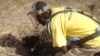 Cons Wani, who works with the Danish Demining Group, brushes dirt away to reveal a rocket-propelled grenade that was found in the center of Bentiu, in South Sudan. (VOA/Bonifacio Taban)