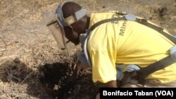 Cons Wani, who works with the Danish Demining Group, brushes dirt away to reveal a rocket-propelled grenade that was found in the center of Bentiu, in South Sudan. (VOA/Bonifacio Taban)